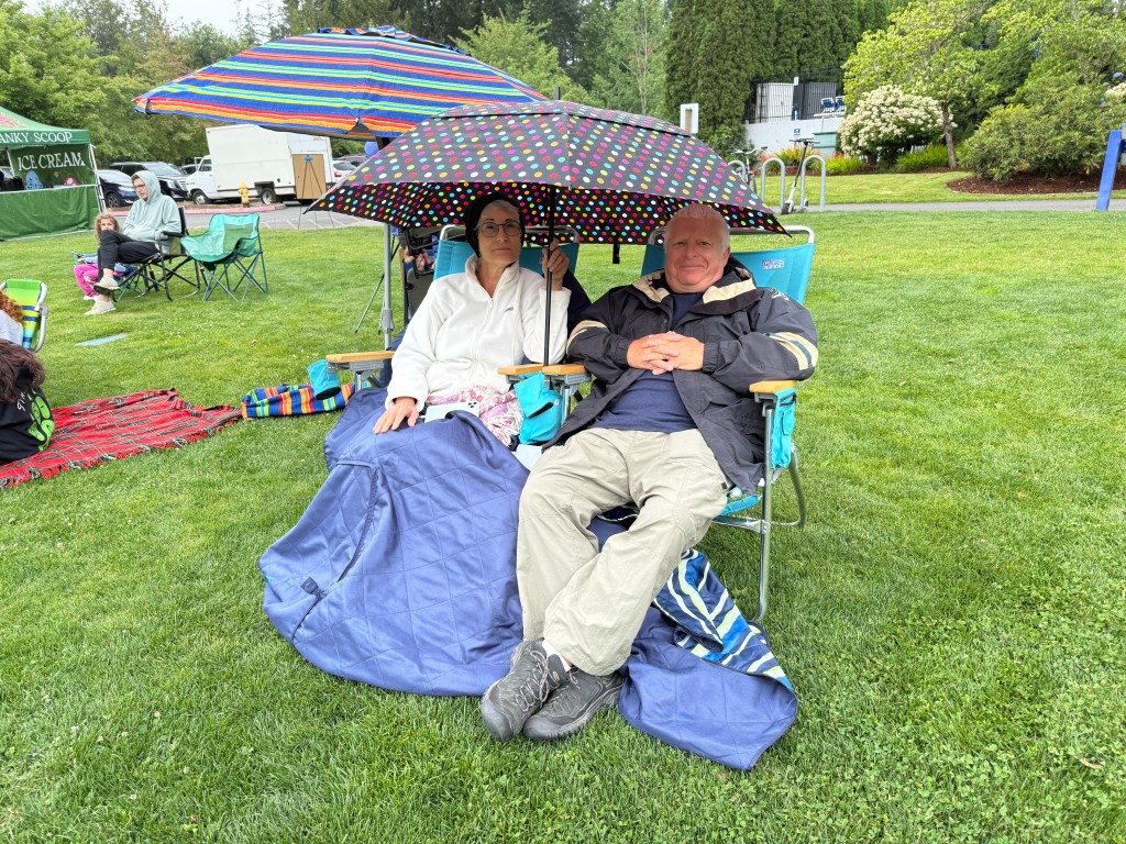 Photo of Couple enjoying the July 16, 2026 performance, with umbrellas to keep of the misty rain.
